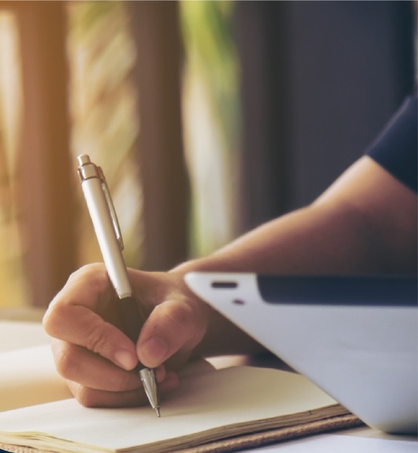 A researcher developing ideas in a notebook beside a laptop